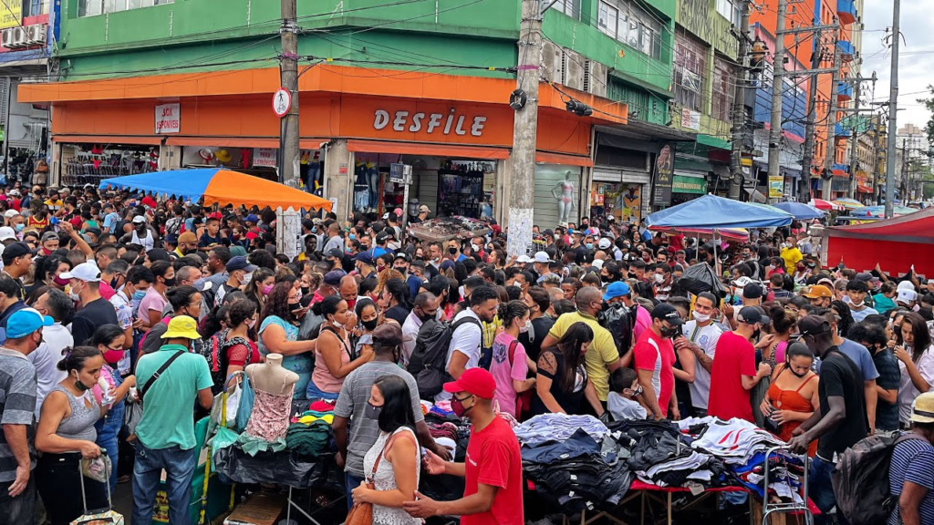 Movimento de pessoas em frente a uma banca e lojas de roupas no Brás em São Paulo